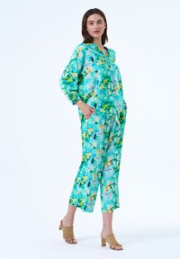 Bloemenprint loungekleding in turkoois, groen en gele tinten. Longsleeve top met een comfortabele pasvorm, bijpassende taps toelopende broek met zakken.
