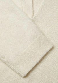 Maglione beige chiaro con scollatura a V, texture a maglia e polsini a coste. Il tessuto appare morbido e leggermente melangiato, mettendo in risalto i raffinati dettagli.