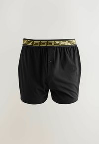 Schwarze Baumwoll-Boxershorts mit einem elastischen Bund in gelbem griechischem Schlüssel-Muster und einem einzelnen Knopf an der Vorderseite.