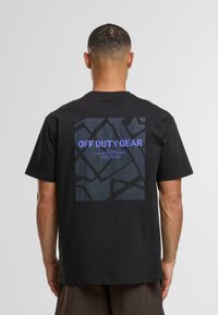 Černé bavlněné tričko s velkým potiskem na zádech obsahujícím texturovaný, tmavý vzor a modrý nápis "OFF DUTY GEAR."