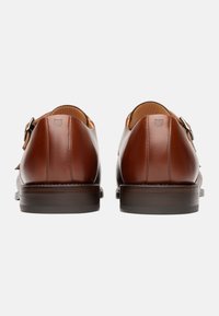 Chaussures en cuir marron avec un design épuré, présentant une texture lisse, un bout arrondi et un accent de boucle subtil ; talon en bois bas.