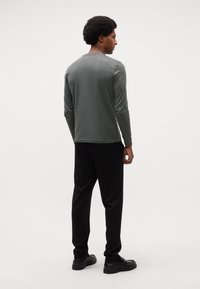 Maglione a maniche lunghe di colore verde oliva, con girocollo, abbinato a pantaloni neri. Tessuto morbido, design aderente, semplice senza motivi o accenti visibili.