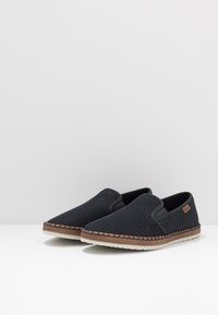 Chaussures slip-on de marine avec une tige en mesh et des panneaux latéraux en textile. Elles présentent une semelle légère avec des détails tressés et une étiquette d'accent marron.