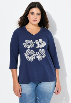 T-shirt bleu marine à manches 3/4 avec un col en V. L'avant présente un graphisme de formes florales en blanc avec divers motifs et textures.