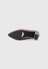 Light pink suede pump with a pointed toe, a slim heel, and a textured black rubber sole. Features a logo detail on the sole.
