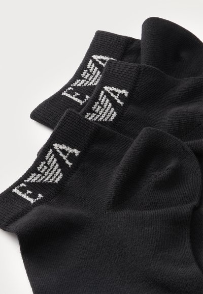 Trois paires de chaussettes noires avec texte et logo blancs sur les bords, pliées soigneusement sur un fond clair.