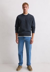 Ciemnoszara bluzka z okrągłym dekoltem i ściągaczami na rękawach, zestawiona z jasnoniebieskimi dżinsami o prostym kroju i beżowym obuwiem. Prosty design i dopasowanie.