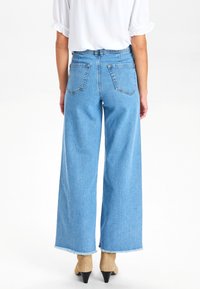 Ljust blå, vida denimjeans med fransad fåll och två bakfickor. Kombination med beige spetsiga klackar.