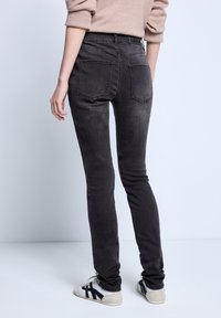 Jeans skinnies negros de cintura alta, con bolsillos traseros y una textura deslavada. El modelo lleva zapatos con un diseño en blanco y negro.