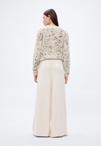 Robustní pletený svetřík v krémové barvě s hnědými skvrnkami, doplněný lehkými, širokými kalhotami v offwhite barvě s volným střihem.