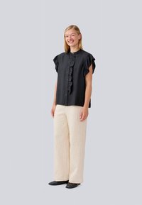 Zwarte blouse met korte mouwen en ruches, met een knopenvoorzijde, gecombineerd met crèmekleurige, gestructureerde broek met wijde pijpen en zwarte instappers.