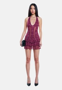 Abito halter in pizzo color bordeaux con pannelli trasparenti e orlo arricciato. Modella che tiene una piccola borsa nera, indossando tacchi neri.