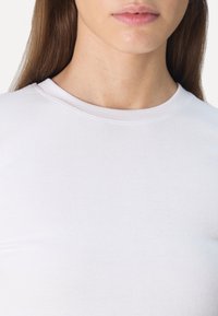 Hvit ribbestrikket t-skjorte med rund hals, teksturert stoff og en tettsittende design. Fokuset er på overkroppsområdet.