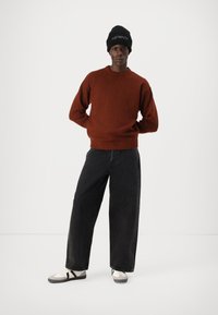 Pull rouille avec un col rond, associé à un jean noir ample et des baskets blanches avec des accents noirs. Bonnet noir.