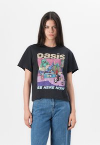 T-shirt nera in cotone con un design cropped, caratterizzata da una grafica colorata di una scena in piscina e il testo "Oasis Be Here Now" in caratteri in grassetto.
