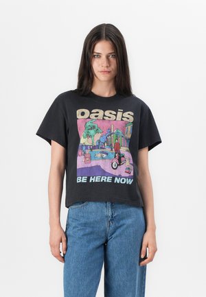 Juodas medvilnės marškinėliai su trumpu dizainu, vaizduojantys spalvingą baseino sceną ir užrašą „Oasis Be Here Now“ ryškiomis raidėmis.