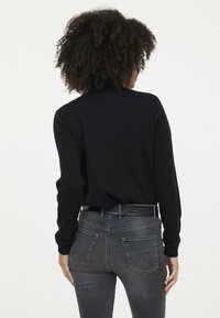 Haut à manches longues noir avec texture côtelée, associé à un jean slim gris foncé avec poches arrière et détail de couture décorative.