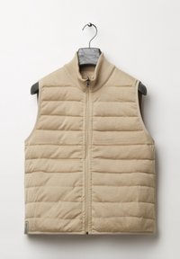 Beige värillinen toppaliivi, jossa korkea kaulus, vaakasuora tikattu kuvio, etuvetoketju ja ilman hihoja. Ripustettuna mustaan henkariin.