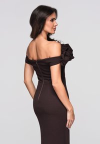 Braunes, schulterfreies, figurbetontes Kleid mit gerafftem Ärmel, glatter Textur und verdecktem Reißverschluss auf der Rückseite. Strukturierter Schnitt betont die Form.