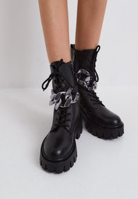 Černé kožené kotníkové boty s masivními podrážkami, se stříbrnými řetězovými detaily, šněrováním v přední části a bočním zipem pro snadné obouvání.