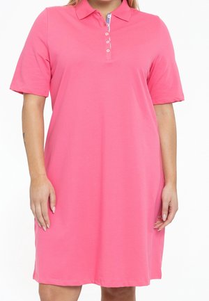 Kobieta ubrana w różową sukienkę polo z krótkim rękawem, kołnierzykiem i czterema guzikami z przodu na białym tle.