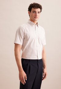 Camicia a maniche corte a quadri di colore beige chiaro con dettagli bianchi, con colletto e bottoni, abbinata a pantaloni blu scuro per un aspetto elegante.