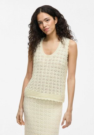 Top de punto en crema pálido con un patrón de espiga y bordes con volantes, presenta un escote redondeado y un dobladillo acanalado. Tejido suave y texturizado.