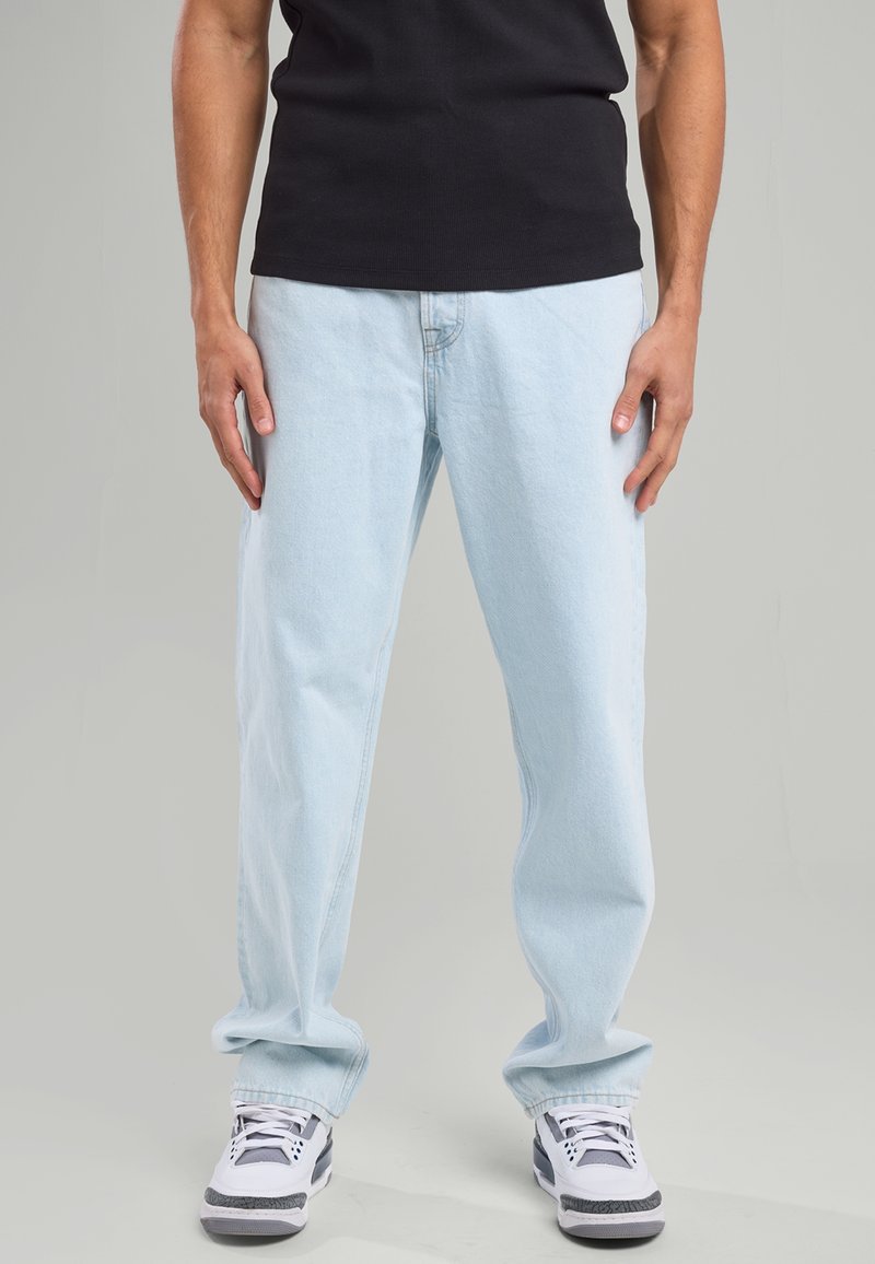 Vaaleansiniset farkut rentoa istuvuutta, joissa on perinteinen viiden taskun design. Yhdistetty mustaan t-paitaan ja valkoisiin lenkkareihin.