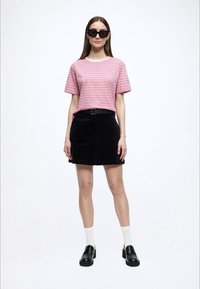 Ροζ και λευκή ριγέ κοντομάνικη μπλούζα συνδυασμένη με μαύρη φούστα από κορντόρι, μαύρα παπούτσια και λευκές κάλτσες. Τα γυαλιά ηλίου προσθέτουν μια μοντέρνα πινελιά.