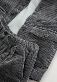 Grijze corduroy blouse met bijpassende sweatpants. De blouse heeft donkere knopen en zakken, terwijl de broek een elastische tailleband en textuur heeft.