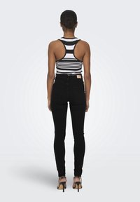 Vaqueros negros de talle alto combinados con una camiseta sin mangas a rayas negras y blancas con diseño de espalda nadadora. El conjunto se completa con sandalias de tacón alto.