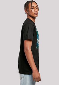 Black cotton t-shirt with short sleeves, featuring turquoise graphic text on the front. Straight fit with a classic crew neckline.