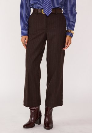 Pantaloni larghi a righe marroni con vita alta, abbinati a una cintura marrone e stivaletti alla caviglia bordeaux, realizzati in un materiale lucido e liscio.