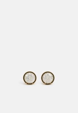 Gold-tone stud earrings featuring round clear crystals encircled by a black rim, with the brand name "GUESS" on the base.