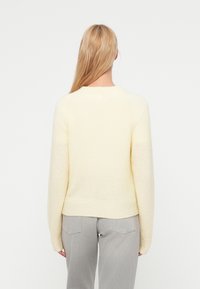 Απαλό, πλεκτό πουλόβερ σε ανοιχτό κίτρινο χρώμα με μακριά μανίκια και στρογγυλή λαιμόκοψη, με εφαρμοστή μέση και υφή στο ύφασμα.