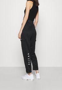 Černé cargo kalhoty s volným střihem, které mají boční kapsy a bílé značení Nike na levé noze. Doplněné bílými teniskami.