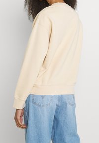Sweatshirt beige à col rond, poignets et ourlet côtelés, avec une coupe ample. Associé à un jean denim bleu clair.
