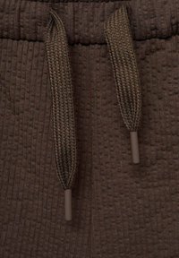 Tissu texturé marron foncé avec un motif à côtes, équipé de cordons tressés et d'embouts en plastique pour le réglage.