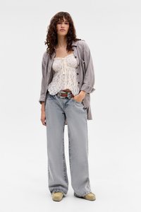 Camisola in pizzo con scollatura arricciata, indossata sotto una camicia oversize a quadri. Abbinata a jeans a gamba larga e scarpe chiare.
