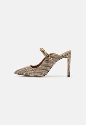 Beige glitter slingback pump met een spitse neus, met een juwelenband en een slanke hoge hak. Gestructureerde stof bedekt het bovenwerk, waardoor visueel belang wordt toegevoegd.