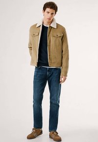 Jachetă din piele întoarsă de culoarea bronzului, cu guler de blană, două buzunare pe piept, asortată cu blugi albastru închis și adidași maro. Design simplu, casual.