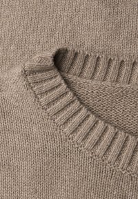 Beige stickad tröja med ribbad krage och fåll, som har en mjuk textur och jämn sömnad genom hela tyget.