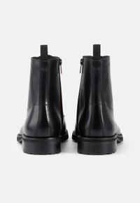 Cizme negre din piele, până la gleznă, cu o textura netedă, fermoare laterale și taburi pentru a le trasa la spate. Talpa robustă din cauciuc negru oferă o aderență sporită.