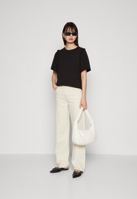 Svart kortermet topp med volanger, kremfargede vide bukser, svarte spisse flats, og en hvit hobo veske. Minimalistisk stil.