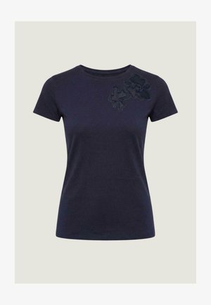 Camiseta femenina de manga corta en azul marino con cuello redondo y dos apliques florales oscuros en la parte superior izquierda del pecho.