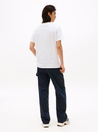 Witte katoenen t-shirt met ronde hals, gecombineerd met marineblauwe cargobroek met zakken, getoond vanaf de achterkant met een minimale achtergrond.