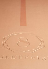 Perzikkleurige lederen oppervlak met een afgestempelde achthoekige design met het cijfer 8; subtiele textuur en een verticale accentstreep.