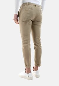 Chino beige con una vestibilità slim, dotati di tasche posteriori e orli arrotolati, abbinati a sneakers bianche su uno sfondo neutro.