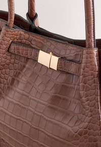 Sac à main en cuir marron à texture croco, avec double poignée et un fermoir rectangulaire doré sur la lanière avant.