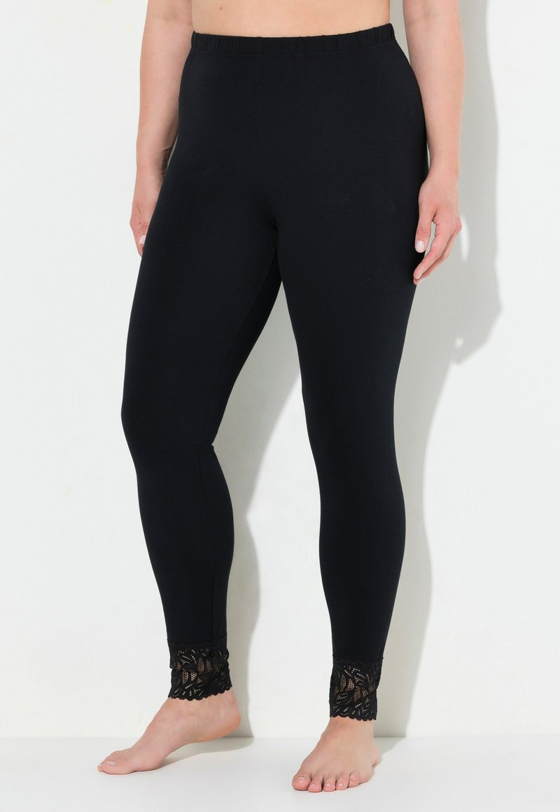 Zwarte leggings van rekbare stof, met een geschulpte kantafwerking bij de enkel. Het ontwerp is strakke pasvorm met een elastische tailleband.